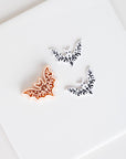 three decorative bat-shaped objects, one orange and two white, arranged on a white surface.