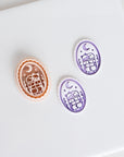 Halloween clay cutter featuring a cat resting on stacked books beneath a crescent moon with two matching purple polymer clay earring pieces.