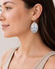 Woman wearing a 35mm Halloween polymer clay earring with crescent moon, cauldron, crystals and botanical details on a silver hook.