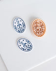Halloween clay earring cutter featuring a crescent moon, steaming cauldron, crystals and foliage with two matching blue and white finished pieces.