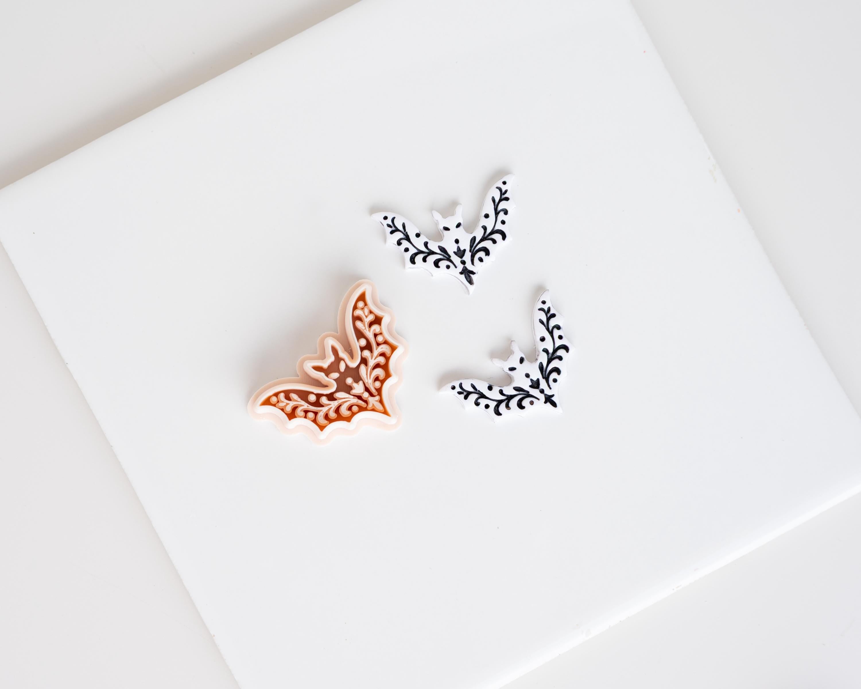 three decorative bat-shaped objects, one orange and two white, arranged on a white surface.