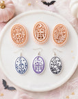 Pastel Halloween flat lay featuring clay cutters and matching earrings with moon, cauldron, cat and stacked books designs for clay earring makers.