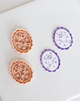 two cookie cutters, one orange and one purple, placed on a white surface.