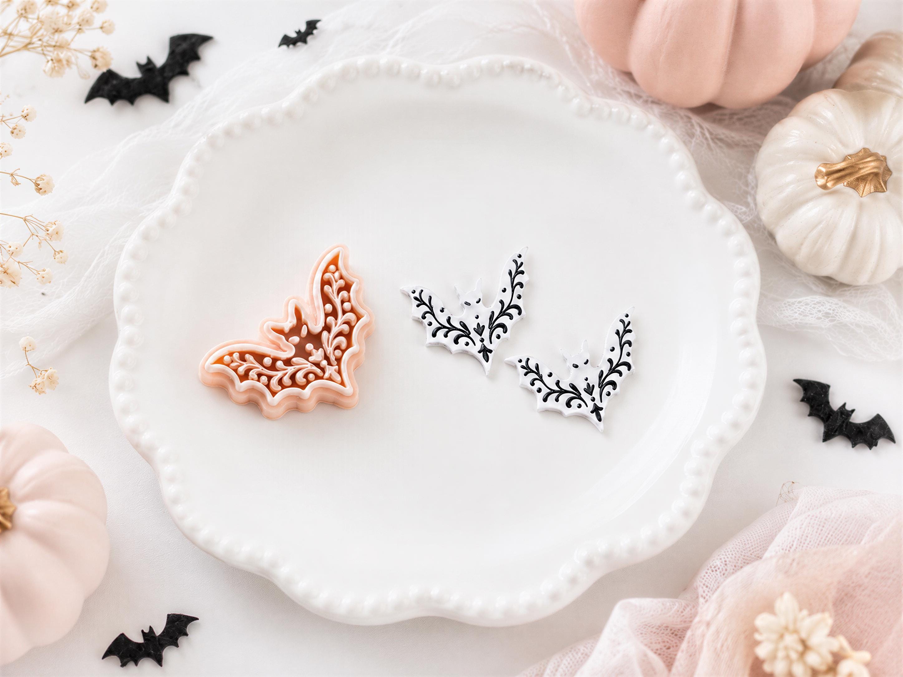 a white plate with two decorative bat-shaped cookies, surrounded by Halloween-themed decorations such as pumpkins and bats.