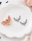 a white plate with two decorative bat-shaped cookies, surrounded by Halloween-themed decorations such as pumpkins and bats.