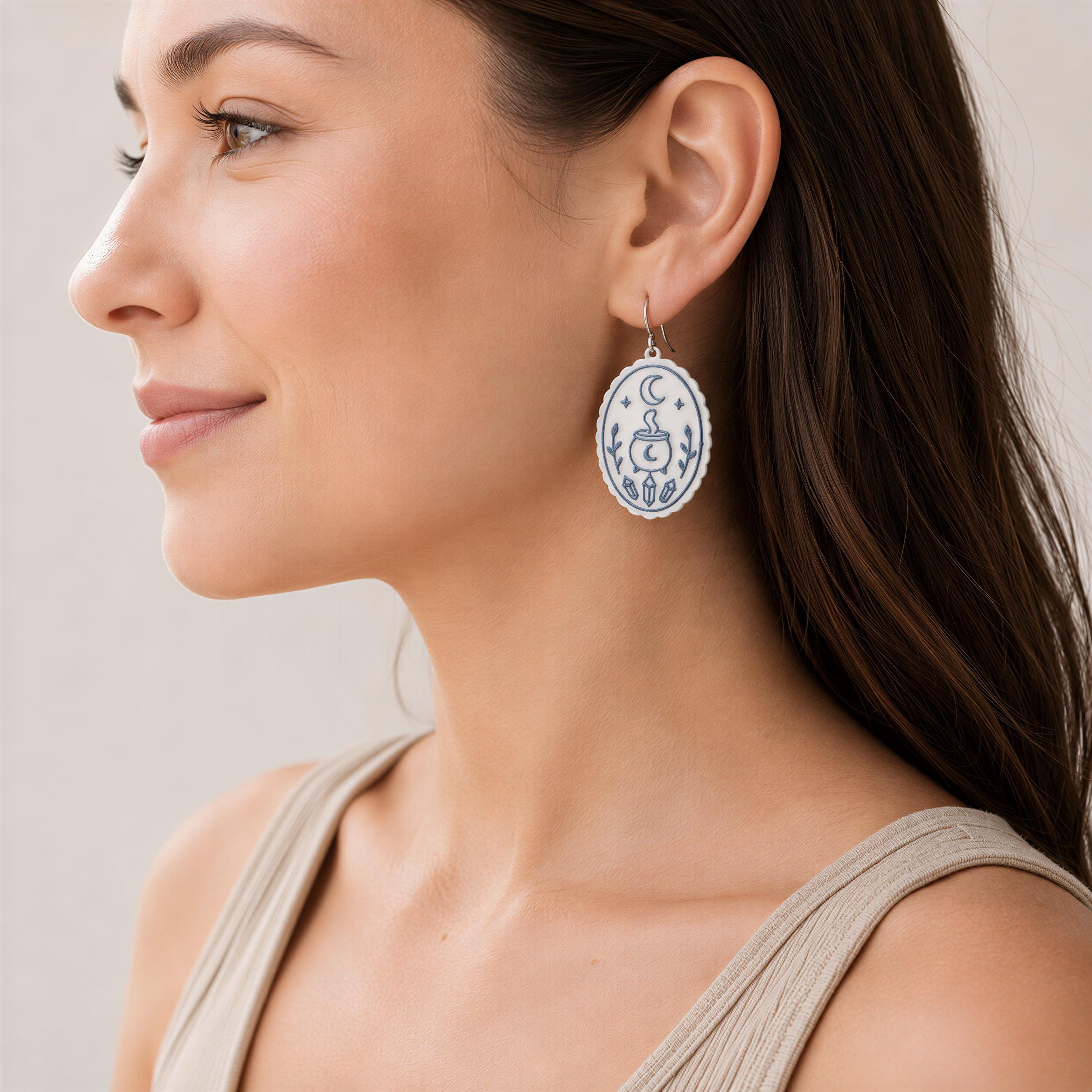 Woman wearing a 35mm Halloween polymer clay earring with crescent moon, cauldron, crystals and botanical details on a silver hook.
